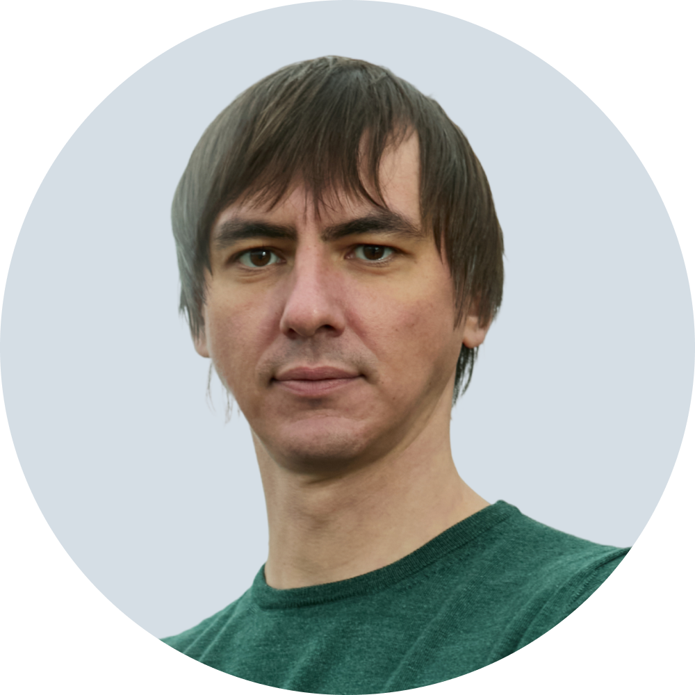 Portrait of a man with short brown hair wearing a green crew-neck shirt against a pale blue circular background.