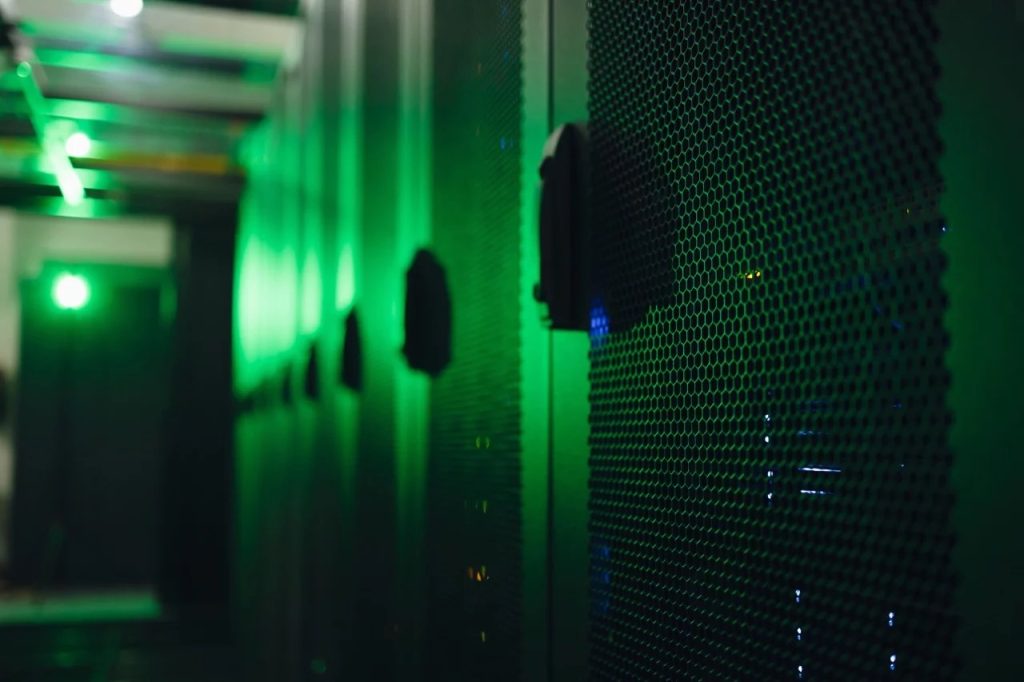 Data center corridor with green lighting and rows of server racks visible along the wall