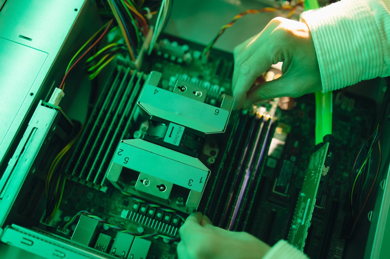 Technician inserts a drive sled into a server backplane in a green-lit server interior.