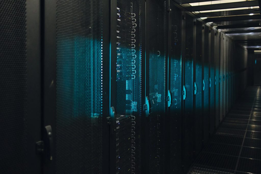 Row of black server racks with blue LED lights in a dim data center corridor.