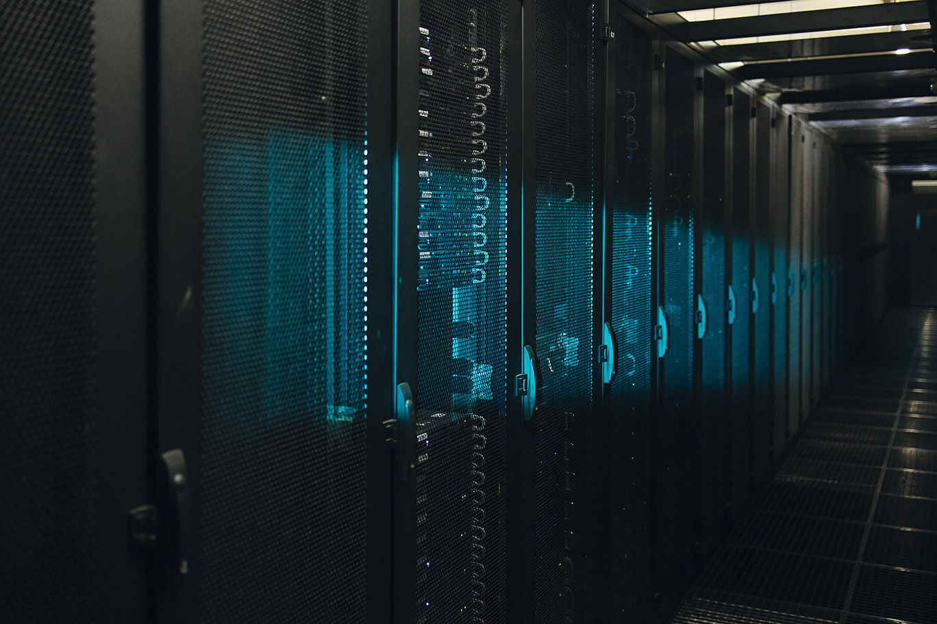 Row of black server racks with blue LED lights in a dim data center corridor.